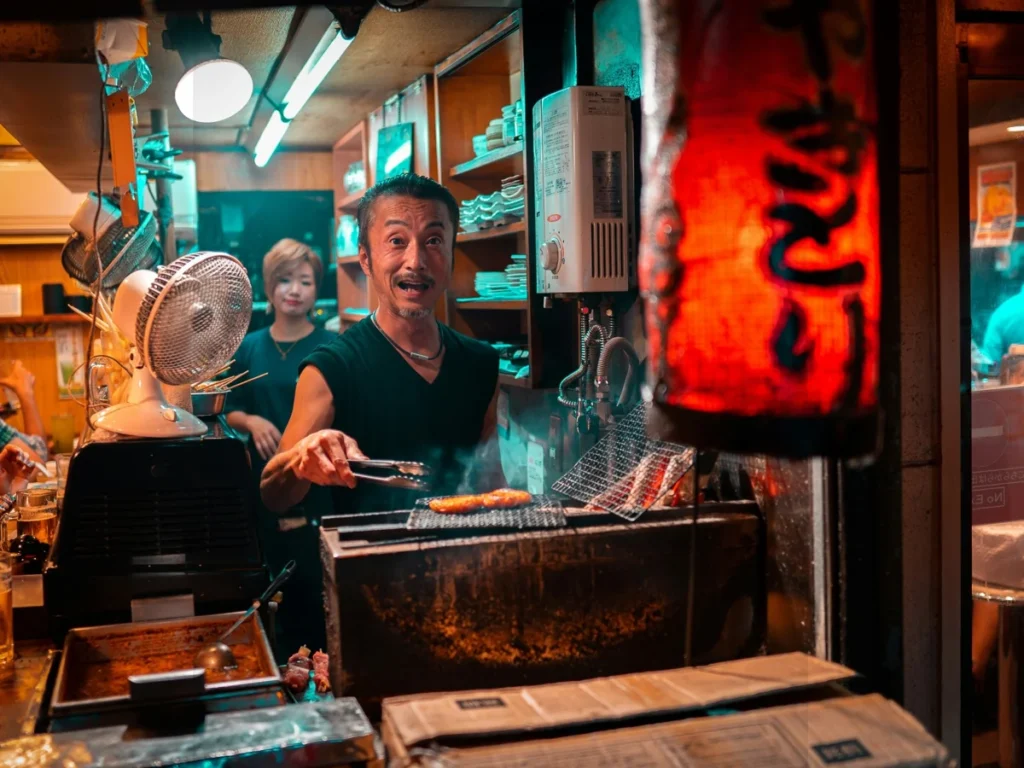 Japanese chef grilling food inside a small izakaya restaurant in Tokyo, representing authentic everyday food culture in Japan.