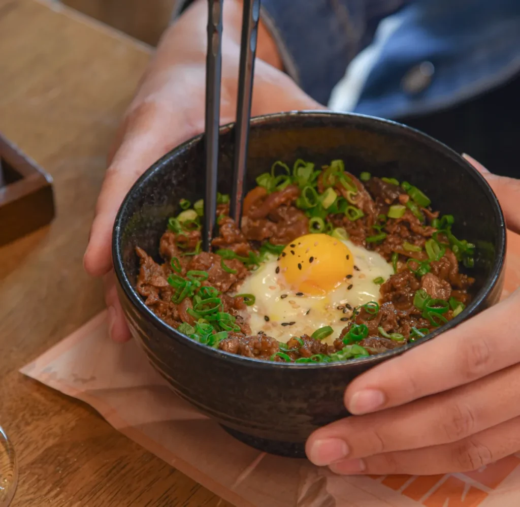 Japanese gyudon beef rice bowl topped with a soft egg and green onions, served in a traditional restaurant.
