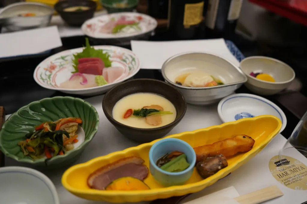 Traditional Japanese kaiseki meal featuring multiple small dishes, sashimi, vegetables, and seasonal ingredients served on a restaurant table.