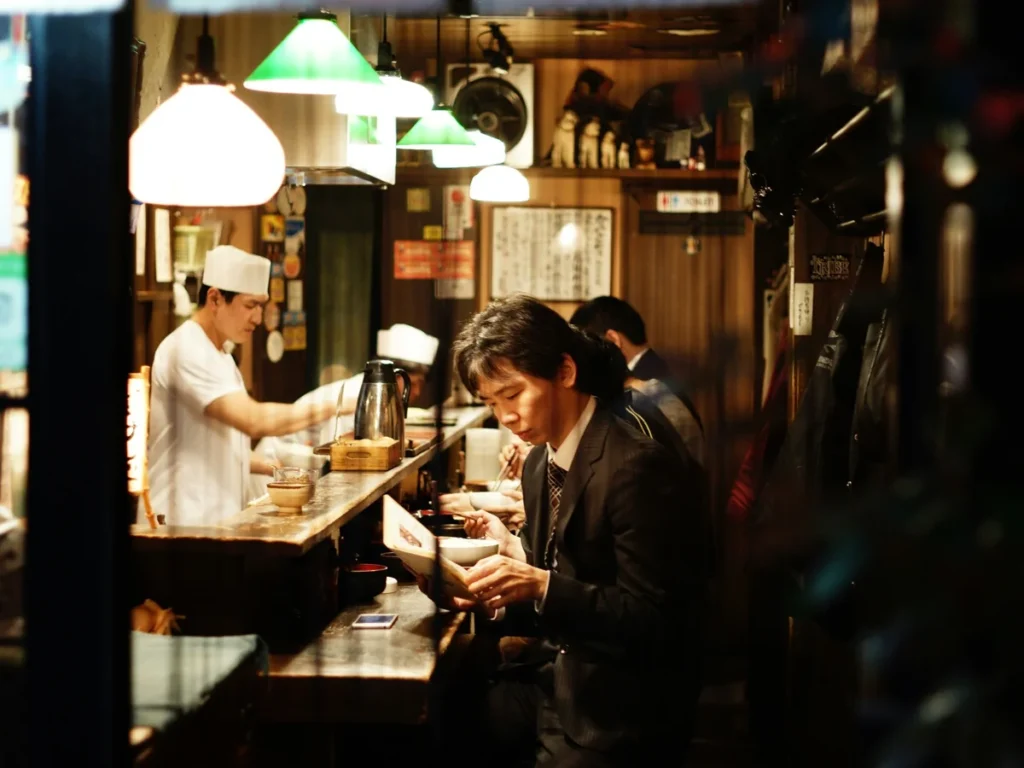 Japanese office worker dining alone at a traditional restaurant counter while a chef prepares food in Tokyo.