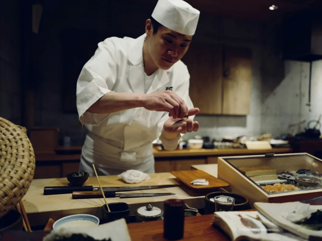 Traditional Japanese sushi chef carefully preparing food at a restaurant counter in Tokyo.